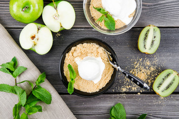 Top view close up Apple crumble dessert with vanilla ice cream, green mint, kiwi on grey wooden...