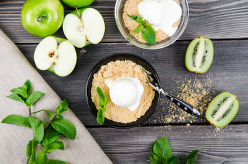 Top view close up Apple crumble dessert with vanilla ice cream, green mint, kiwi on grey wooden table background. fork in cake on tablecloth