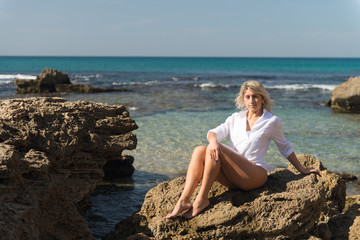 Fototapeta na wymiar white blond female athlete sitting on the rock at the seaside in white shirt