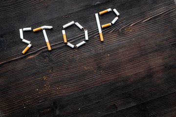 Stop smoking. Word stop lined cigarettes on dark wooden background top view copy space