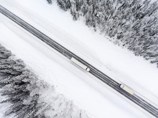 Semitrailer truck and lorry driving from the opposite direction on slippery winter asphalt highway, top view from drone