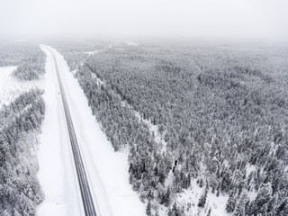 Aerial view at line of slippery winter road at overcast. Taiga is on north of Russia