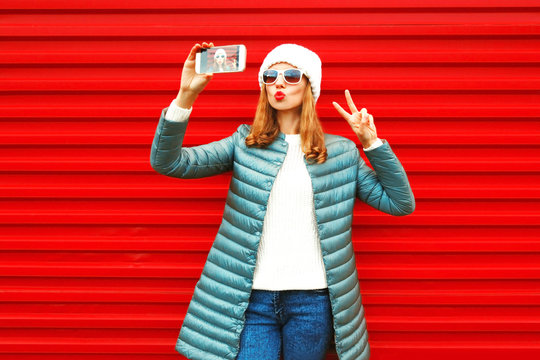 Fashion pretty woman takes a picture self portrait on a smartphone on red background
