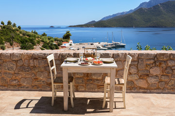 A table served for two with snacks and drinks on the summer terrace of the hotel room by the seascape.