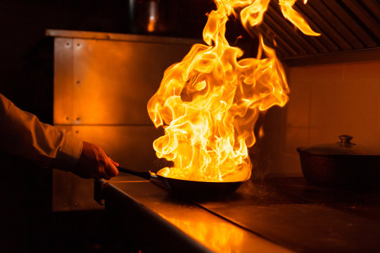 Flambe Lamb Rib Roast. Cooking With Fire In Frying Pan. Professional Chef In A Commercial Kitchen Cooking. Man Frying Food In Flaming Pan On Hob In Outdoor Kitchen. Slow Motion