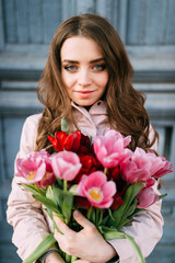 Lovely cute amazing brunette girl standing in front of old vintage blue door with a bouquet of fresh tulips. Women`s day. 8 March. Beautiful teen female holding lots of flowers as gift from boyfriend.