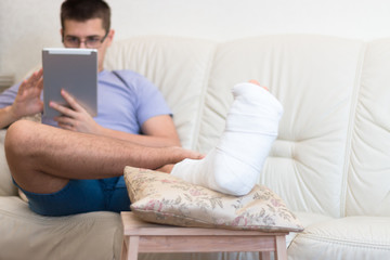 A teenager boy with a broken foot alone at home doing homework, reading. Leg in a cast. Disease. 