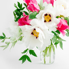 Beautiful bouquet of white peonies and pink tulips in a glass vase on a white background