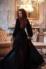 Sensual young woman in a black boudoir dress in classic interior