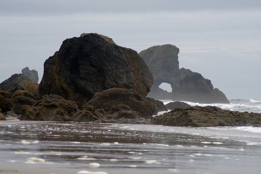 Low angle shot of Rock formations on a otherwise sandy beach on a foggy day. Rough waves are visible. In Cannon Beach, Oregon