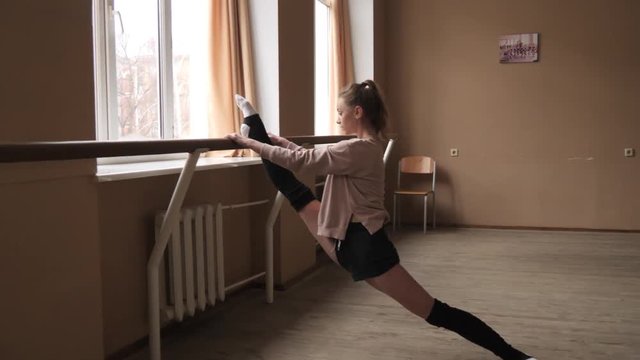 Flexible young woman dancer stretching legs at studio in slow motion