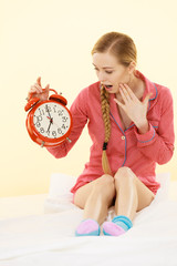 Shocked woman wearing pajamas holding clock