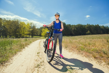 Fototapeta premium One young woman rides on a mountain bike outside of town on the road in the forest on a summer day.