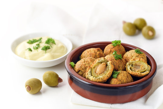 baked olive balls in parmesan dough coat with a creamy garlic sauce, spanish tapas appetizer in a typical ceramic bowl on a white napkin, copy space