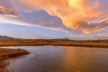 Winter Sunset Clouds - Colorful sunset clouds rolling over a frozen mountain lake at foothill of front range of Rocky Mountains. Bear Creek Park, Denver-Lakewood, Colorado, USA.