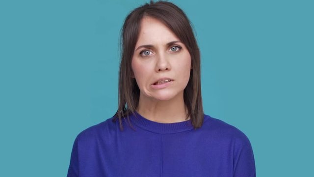 Portrait of caucasian woman feeling anger and annoyance trying to keep calm pretending she express kindness over blue background. Concept of emotions
