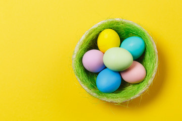 Fototapeta na wymiar Six colorful pastel monophonic painted Easter eggs in basket with green grass isolated on yellow background. Happy Easter concept. Copy space for advertisement. With place for text. Top view on eggs.