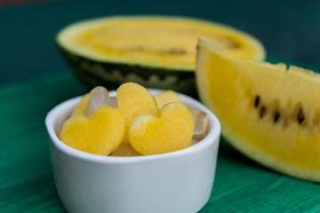 Sweet honey yellow watermelon heart shaped pieces, served with ice in white bowl, on green background