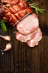  Sliced smoked gammon  on a wooden  table with addition of fresh  herbs and aromatic spices.  ...