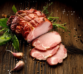  Sliced smoked gammon  on a wooden  table with addition of fresh  herbs and aromatic spices.  ...