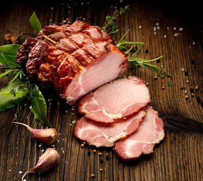  Sliced smoked gammon  on a wooden  table with addition of fresh  herbs and aromatic spices.   Natural product from organic farm, produced by traditional methods