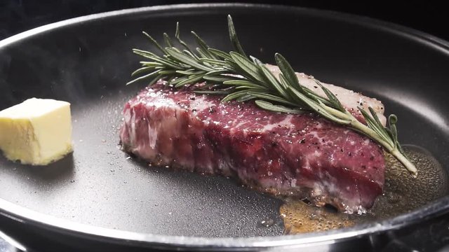 Slices of butter falls on a frying pan to the steak