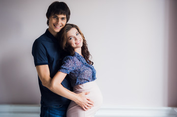 Fototapeta premium Beautiful young couple expecting baby staying in front of wall at home.