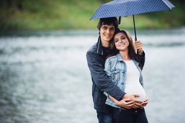 Pregnant woman and man holding an umbrella at the park in the drizzly day outdoors