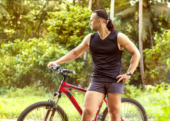 Obraz premium sporty muscular guy with a bicycle standing on the street amidst tropical palm trees