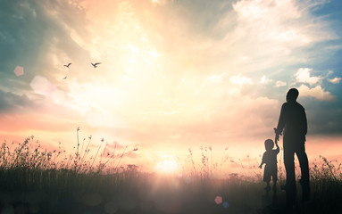 International migrants day concept: Silhouettes father and son holding hand in hand on meadow autumn sunset background