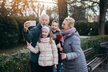 Grandparents taking selfie photo with their grandchildren in city park.