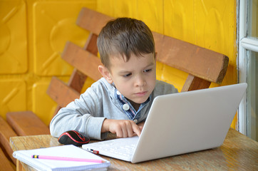 A teenager is sitting at a table in front of a laptop. the boy looks seriously at the computer. working. Outdoors. in the arbor, in the village