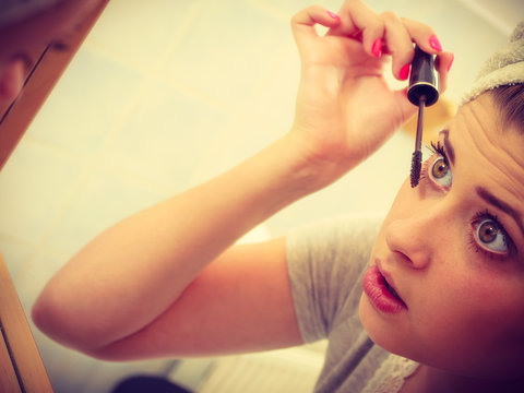 Woman in bathroom applying mascara on eyelashes