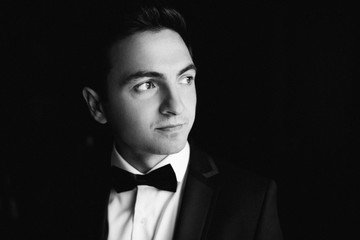 stylish groom smiling, portrait at the window while getting read
