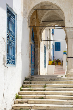 steps to arch with blue window on the street in tunisian town