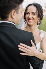 Beautiful happy young bride kissing handsome groom in sunlit par