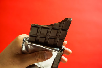 チョコレートを食べる　かじったチョコレートと手　赤色背景