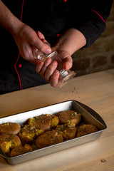 Chef hands cooking potatoes in baking tray with herbs, salt, oil and spices. Step homemade recipe. Food dark wooden background.