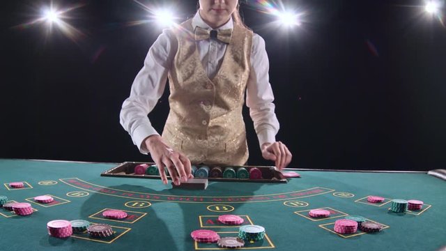 Casino croupier woman mixing the poker cards and performing trick with cards. Black background. Bright light. Slow motion