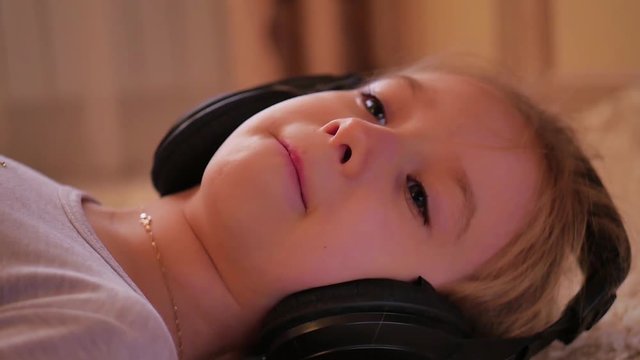 Cheerful young girl listening music in headphones lying on floor at home