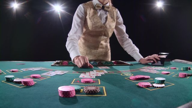 Casino croupier distributes for table poker three cards are the flop. Black background. Bright light. Slow motion