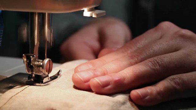 Male sewer working with fabric and thread on sewing machine