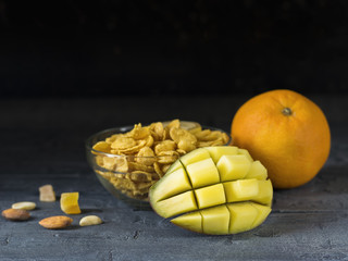 Peeled mango, orange, flakes, and nuts on a dark wooden table.