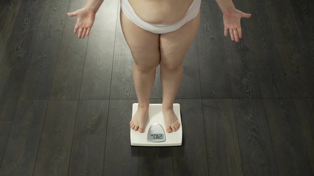 Ineffective dieting, woman with extra body fat weighing herself, dissatisfied