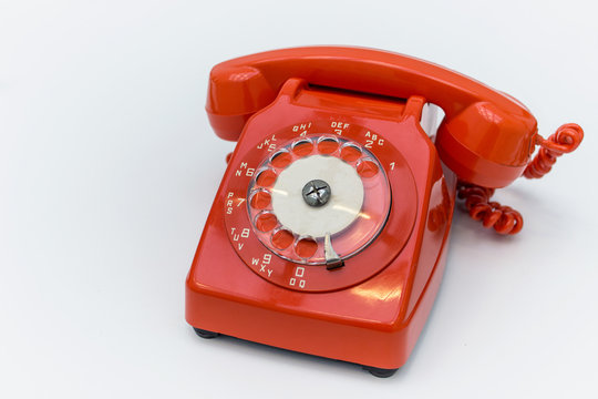 Old fashioned red rotary telephone on white background.