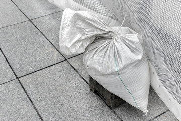 Single sandbag, white plastic bag filled with sand used as a weight to hold construction steady.