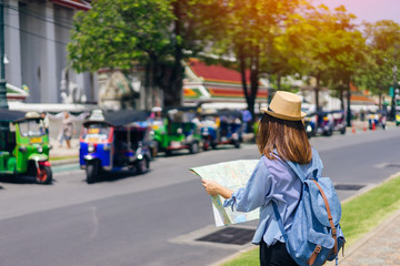 Young woman traveler with sky blue backpack and hat looking map find the way with tuk tuk thailand...