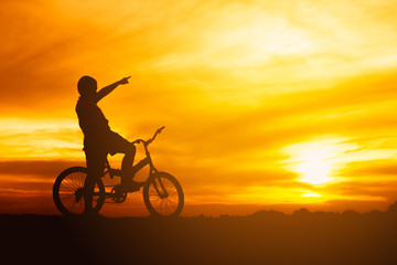 Fototapeta na wymiar silhouette boy riding bicycle at sunset or sunrise background