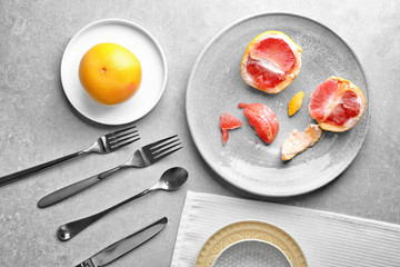 Ceramic plates with grapefruit and cutlery on grey background