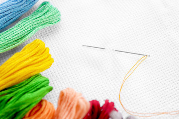 White fabric with colorful threads and sewing needle, closeup